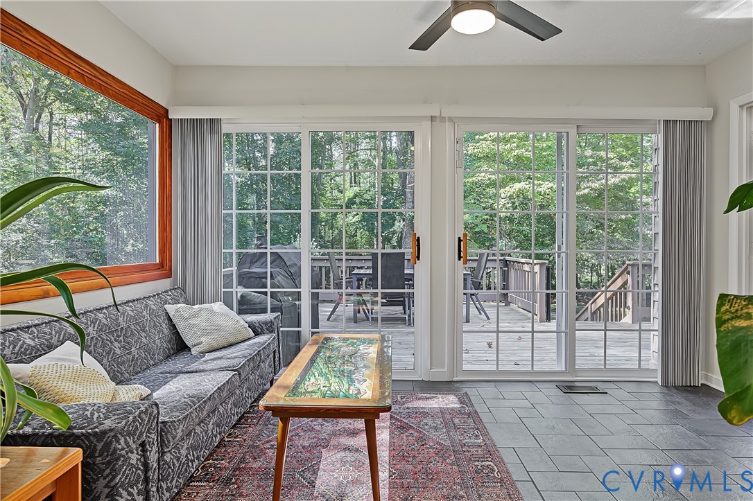 Sunroom featuring grid-pattern sliding glass doors, natural wood window trim, slate-finish tile flooring, and a ceiling fan with integrated lighting