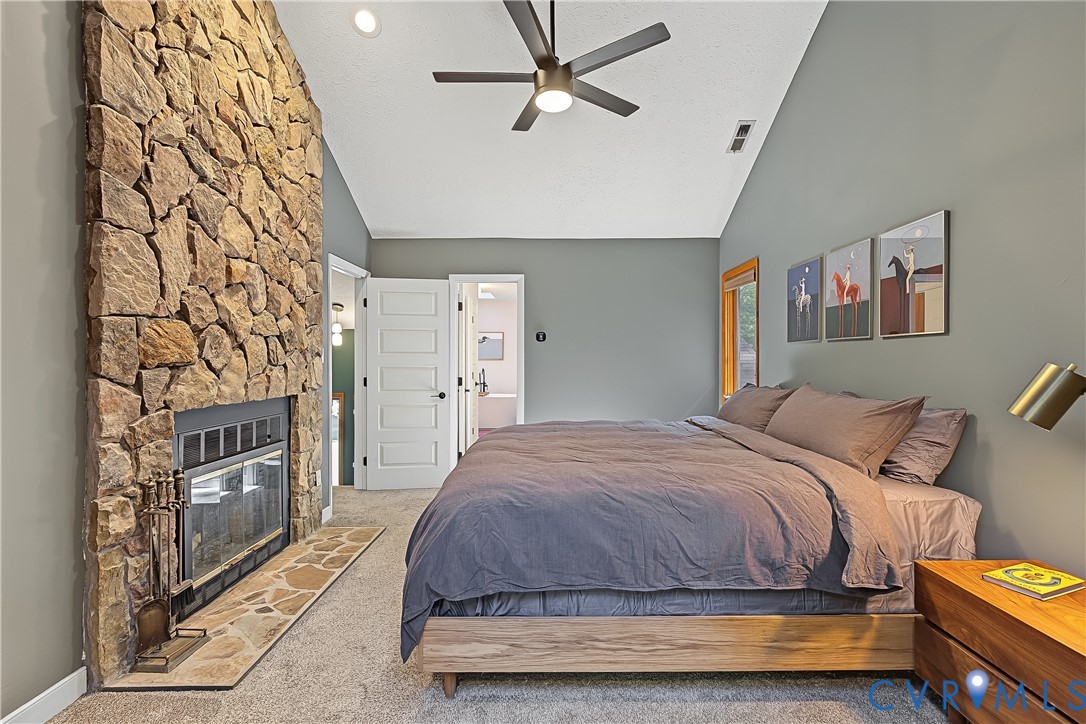 Floor-to-ceiling stone fireplace with a stone hearth, vaulted ceilings, and a ceiling fan