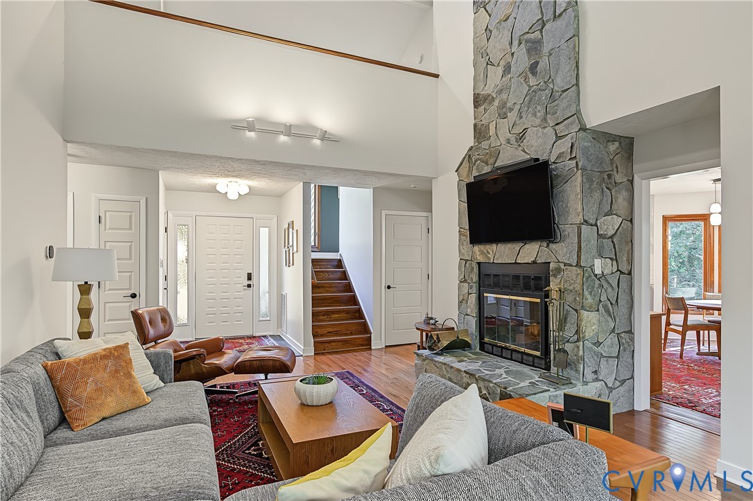 High-ceilinged living area featuring a floor-to-ceiling natural stone fireplace, wood-finish flooring, and a wooden staircase