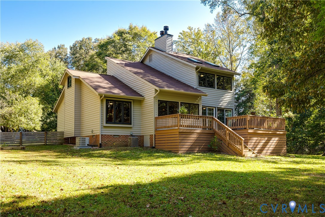 Multi-level residence featuring light-toned horizontal siding, a multi-tiered wooden deck with railings, skylights, and a brick foundation element