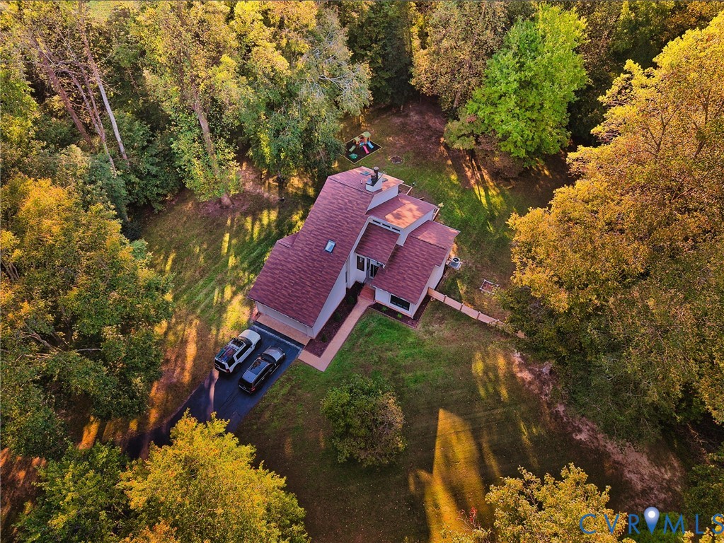 Aerial view of a multi-level residence featuring a pitched roof, an asphalt driveway, and expansive, wooded grounds with mature trees