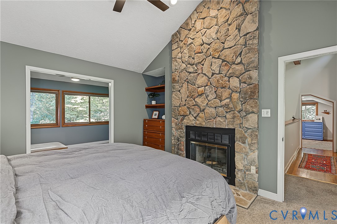Vaulted ceiling with a ceiling fan, full-height natural stone fireplace, and built-in wood shelving