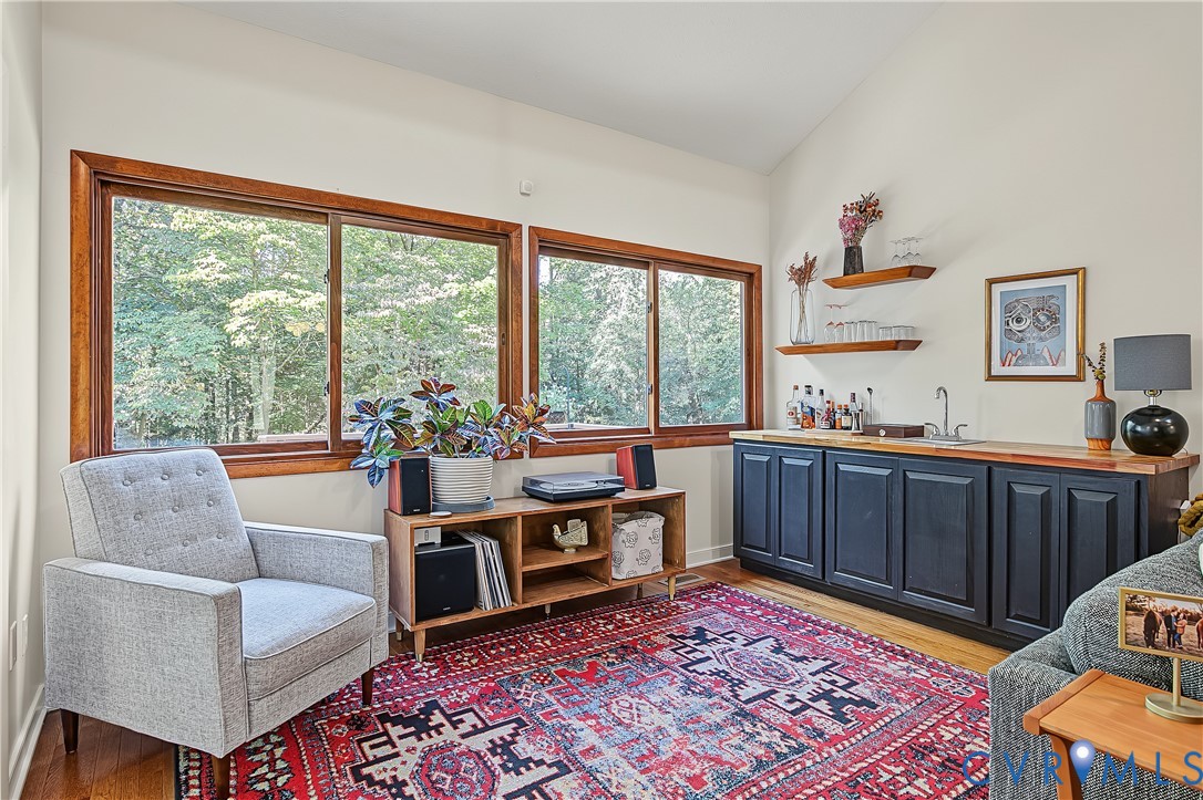 Vaulted ceilings, large windows with wood trim, built-in cabinetry, integrated wet bar with sink, and floating wood shelving