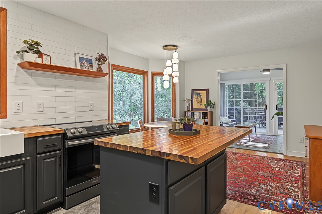 Kitchen featuring a central island with a wood-finish countertop, subway tile backsplash, farmhouse-style sink, floating wood shelf, and multi-light pendant fixture