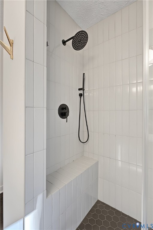 Walk-in shower featuring vertical white subway tile walls, built-in tiled bench, hexagonal floor tiling, and matte black rain-style shower head with coordinating handheld wand