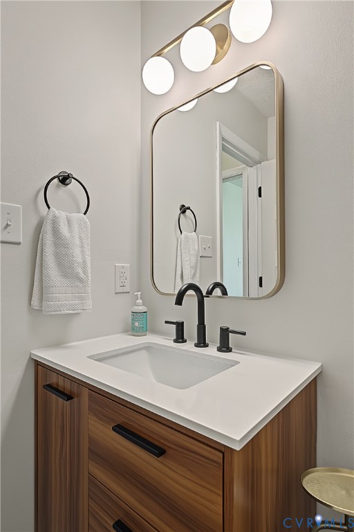 Vanity featuring wood-finish cabinetry, a white countertop, matte black widespread faucet, rectangular mirror with rounded corners, and a three-globe light fixture