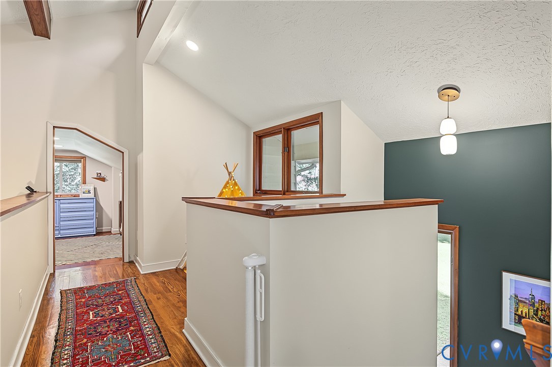 Vaulted ceilings featuring exposed wood beam, hardwood flooring, dual-tone wall treatment, and modern pendant lighting