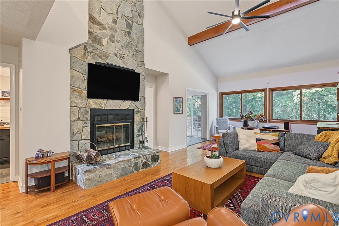 Vaulted ceilings with exposed wood beams, floor-to-ceiling stone fireplace, wood-finish flooring, and expansive windows Vaulted ceilings with exposed wood beams, floor-to-ceiling stone fireplace, wood-finish flooring, and expansive windows