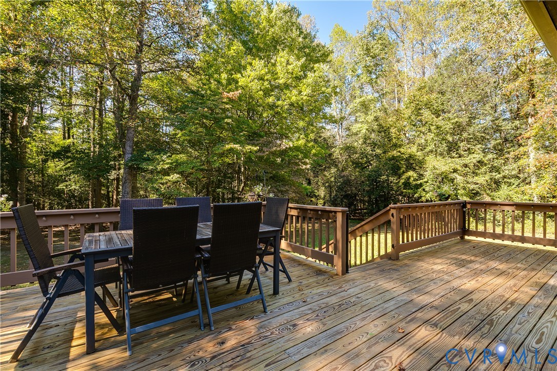 Expansive wood-plank deck featuring a wooden railing and a staircase leading to the rear grounds, framed by mature trees