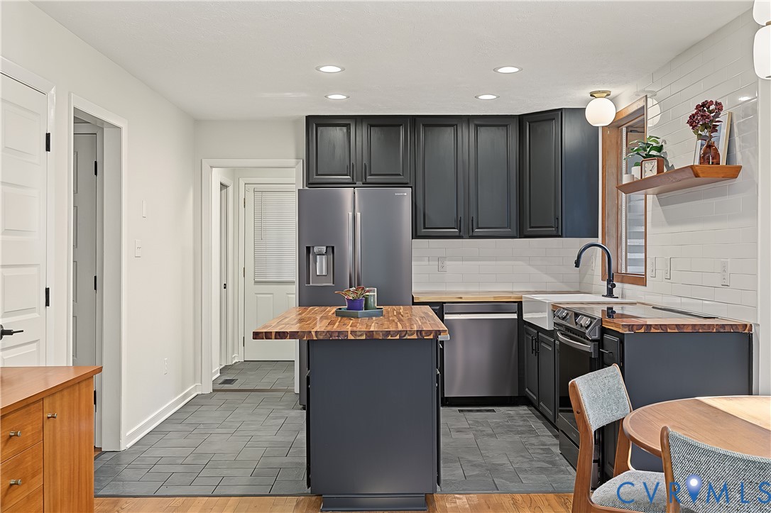 Kitchen featuring dark cabinetry, butcher-block countertops, white subway tile backsplash, farmhouse-style sink, and tile flooring