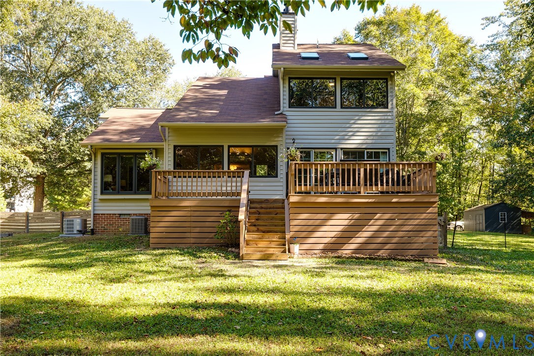 Rear exterior featuring a multi-level wood deck with stairs, a brick and siding facade, skylights, and dark-framed windows
