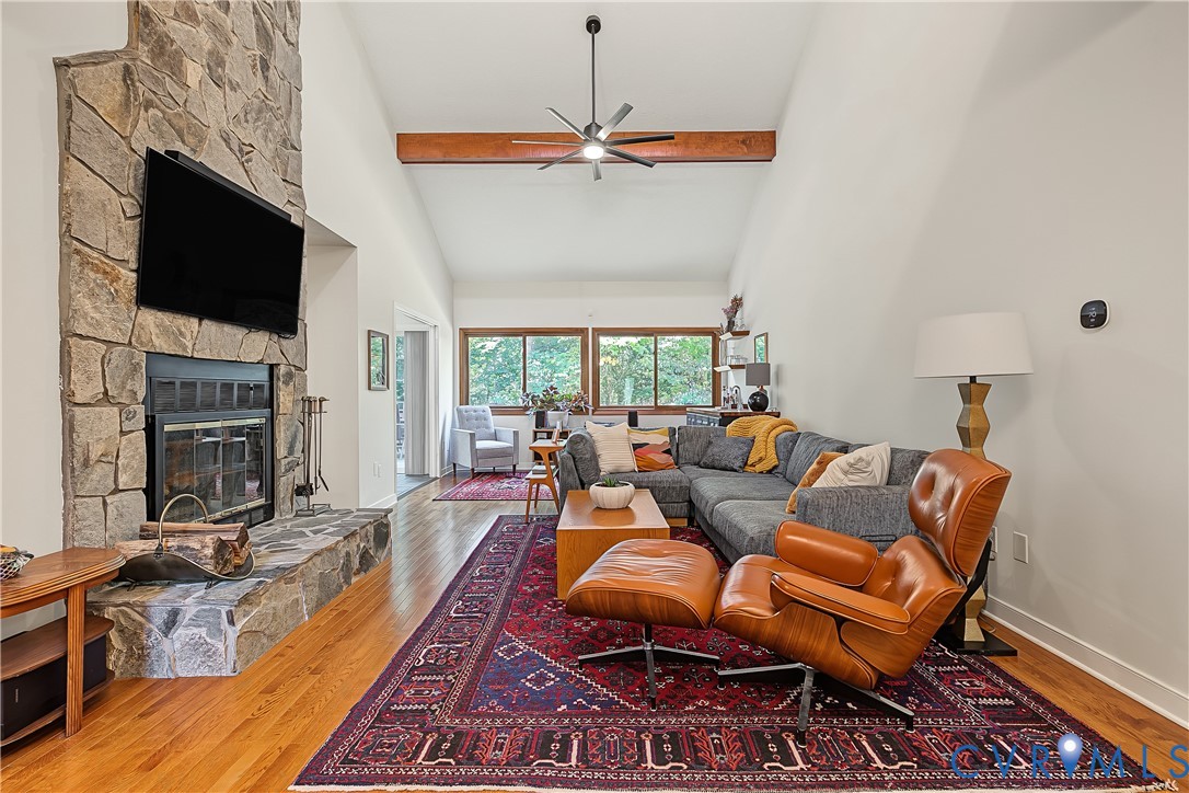 Floor-to-ceiling stone fireplace, vaulted ceilings, exposed wooden ceiling beam, wood-finish flooring, and expansive windows Floor-to-ceiling stone fireplace, vaulted ceilings, exposed wooden ceiling beam, wood-finish flooring, and expansive windows