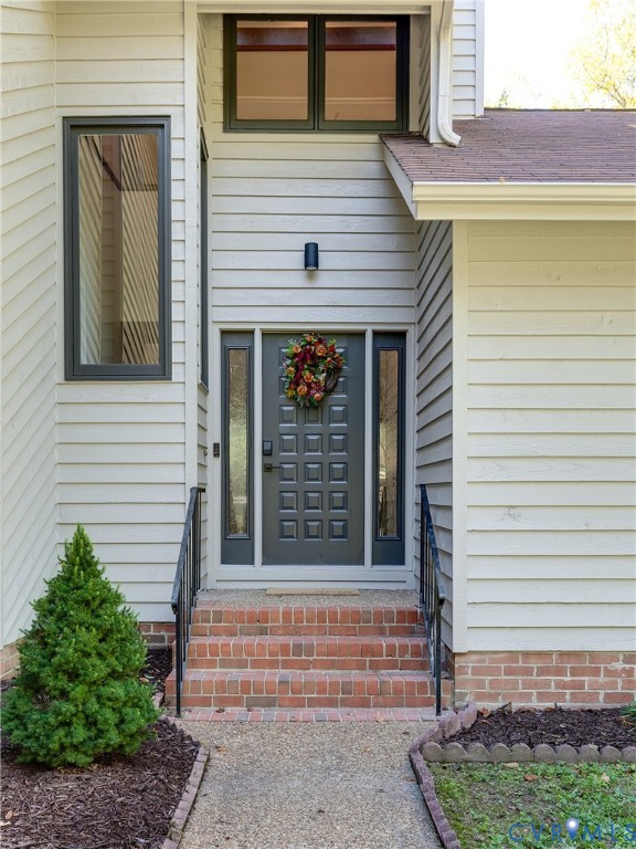 Entryway featuring horizontal siding, brick staircase with metal handrails, paneled door with glass sidelights, and multi-level windows with dark framing Entryway featuring horizontal siding, brick staircase with metal handrails, paneled door with glass sidelights, and multi-level windows with dark framing