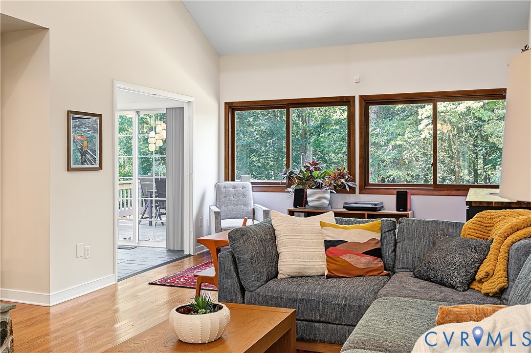 Vaulted ceiling living area featuring wood-finish flooring and expansive windows with natural scenery Vaulted ceiling living area featuring wood-finish flooring and expansive windows with natural scenery