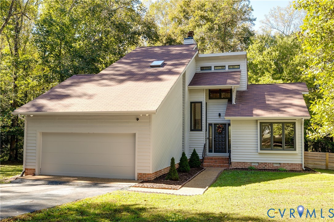Multi-level exterior featuring light-toned horizontal siding, a prominent roofline with a skylight, a brick foundation perimeter, and an attached two-car garage Multi-level exterior featuring light-toned horizontal siding, a prominent roofline with a skylight, a brick foundation perimeter, and an attached two-car garage