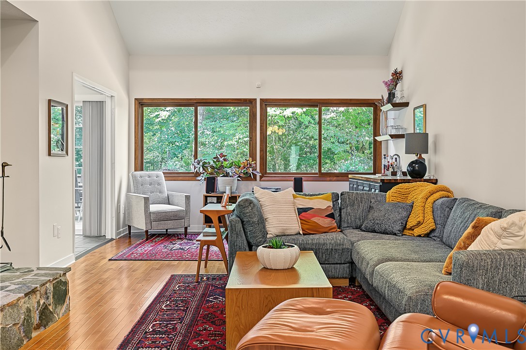 Vaulted ceiling, wood-finish flooring, stone-faced fireplace hearth, and large windows with wood trim Vaulted ceiling, wood-finish flooring, stone-faced fireplace hearth, and large windows with wood trim