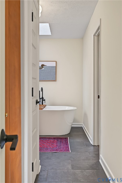 Freestanding soaking tub featuring a matte black floor-mounted faucet and large-format grey tile flooring