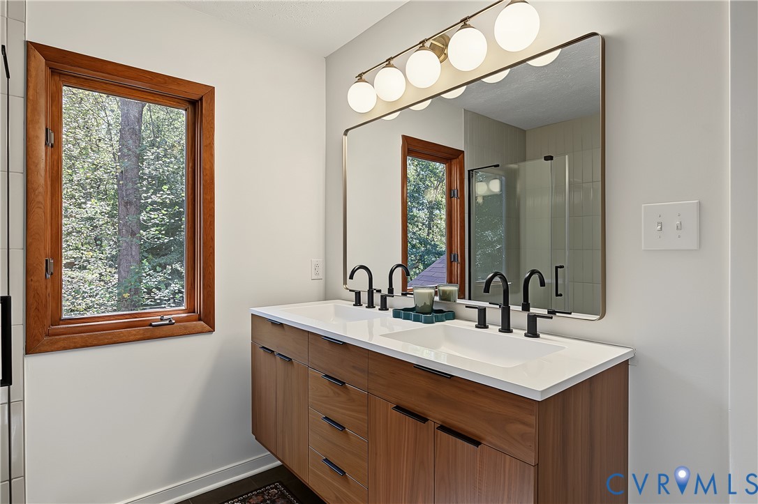 Floating vanity featuring wood-finish cabinetry, a white countertop with integrated dual sinks, matte black widespread faucets, and a multi-globe light fixture