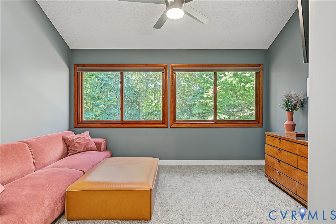 Vaulted ceiling featuring a central lighted ceiling fan, dual windows framed in natural wood, and wall-to-wall carpeting