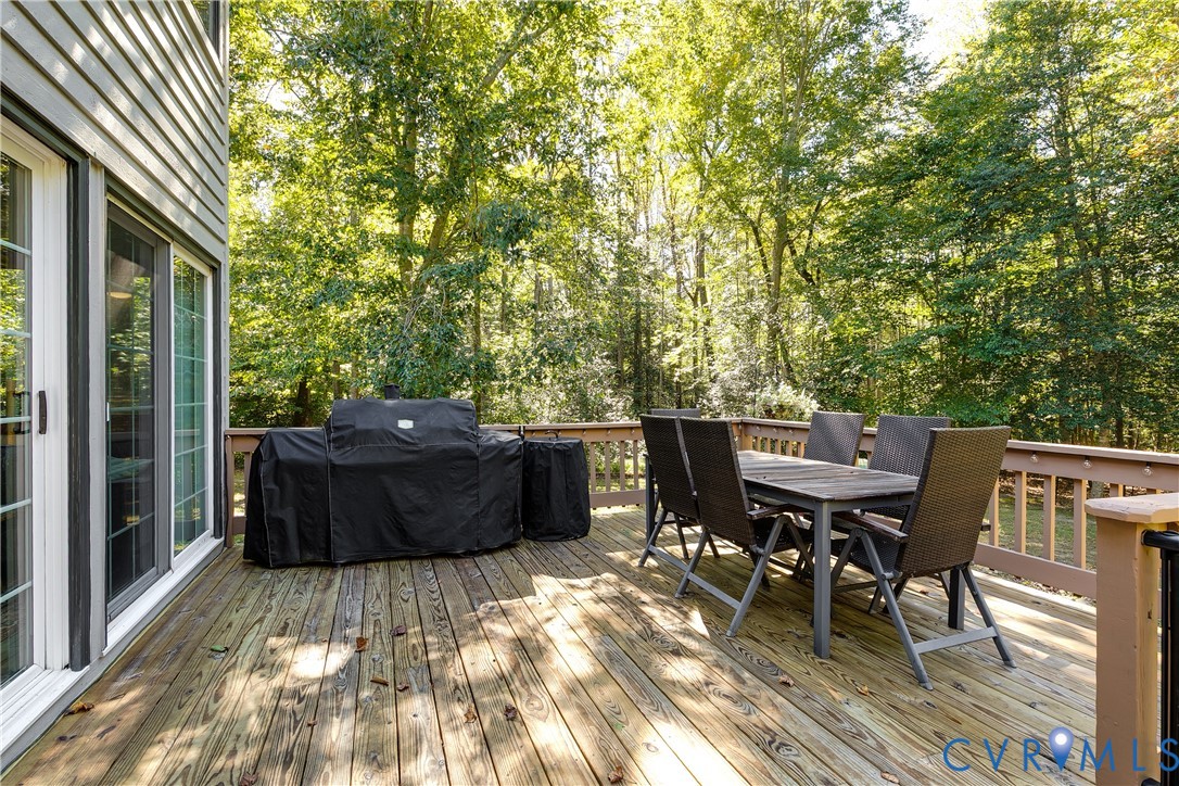 Elevated wooden deck featuring horizontal railings and direct access via sliding glass doors, bordered by mature trees