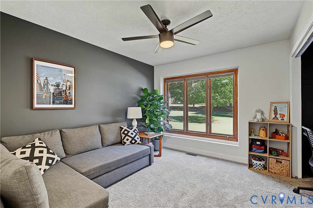 Room featuring a dark-toned accent wall, large picture window with wood trim, ceiling fan with integrated lighting, and neutral carpeting