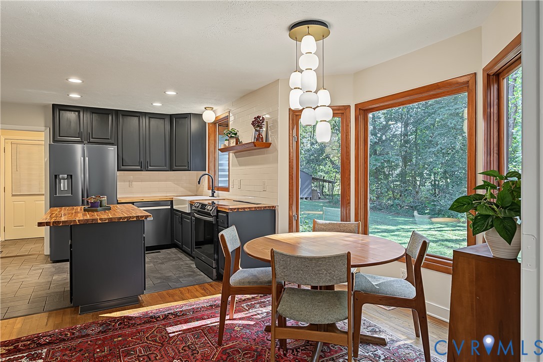 Kitchen featuring dark cabinetry, butcher block countertops, an apron-front sink, multi-pendant lighting, and expansive windows