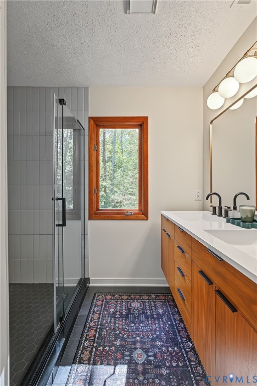 Wood-finish cabinetry with a white countertop and dual undermount sinks, glass-enclosed shower with vertical wall tiling and hexagonal floor tile, and a multi-globe vanity light fixture