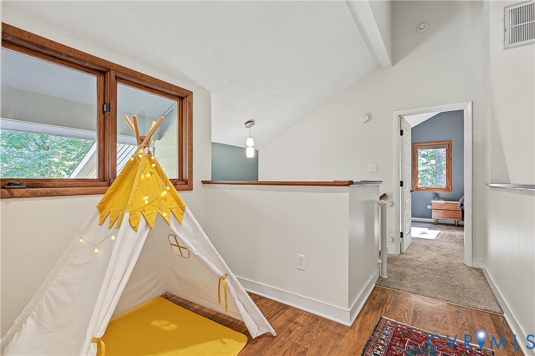 Vaulted ceiling with wood-framed windows, wood-finish flooring, and a half-wall partition with a wood cap