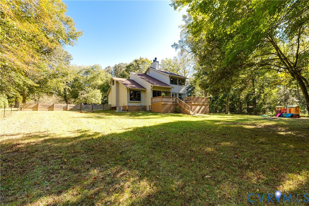 Expansive backyard featuring a leveled grass lawn, mature trees, wood-slat perimeter fencing, and an elevated wood deck