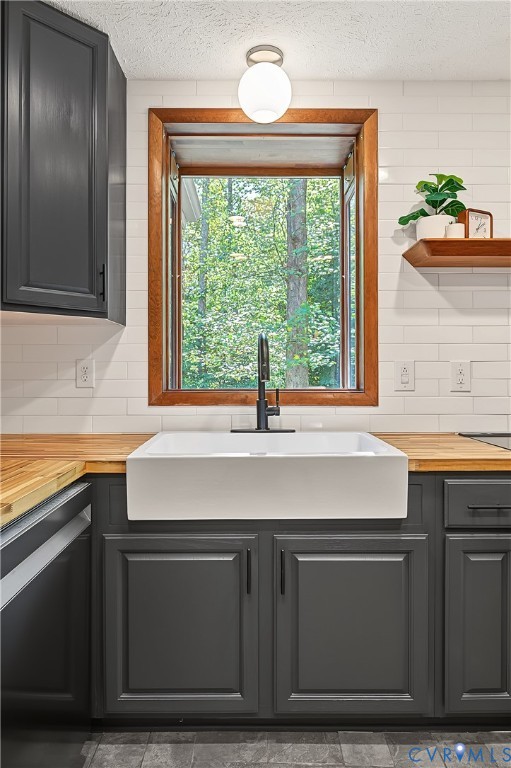 Kitchen featuring a white farmhouse apron-front sink, wood-finish countertops, subway tile backsplash, dark-finished cabinetry, and a globe-style flush mount light fixture