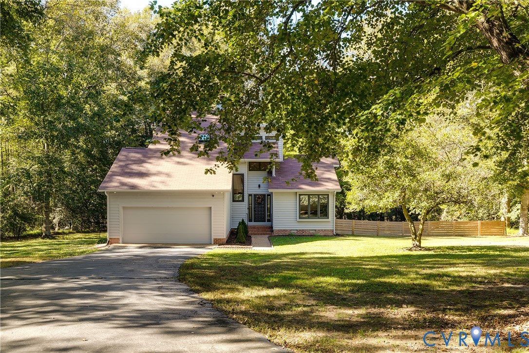 Two-story exterior featuring light-toned horizontal siding, a gabled roofline, an attached two-car garage, and a wood-slat privacy fence on a lot with mature trees Two-story exterior featuring light-toned horizontal siding, a gabled roofline, an attached two-car garage, and a wood-slat privacy fence on a lot with mature trees