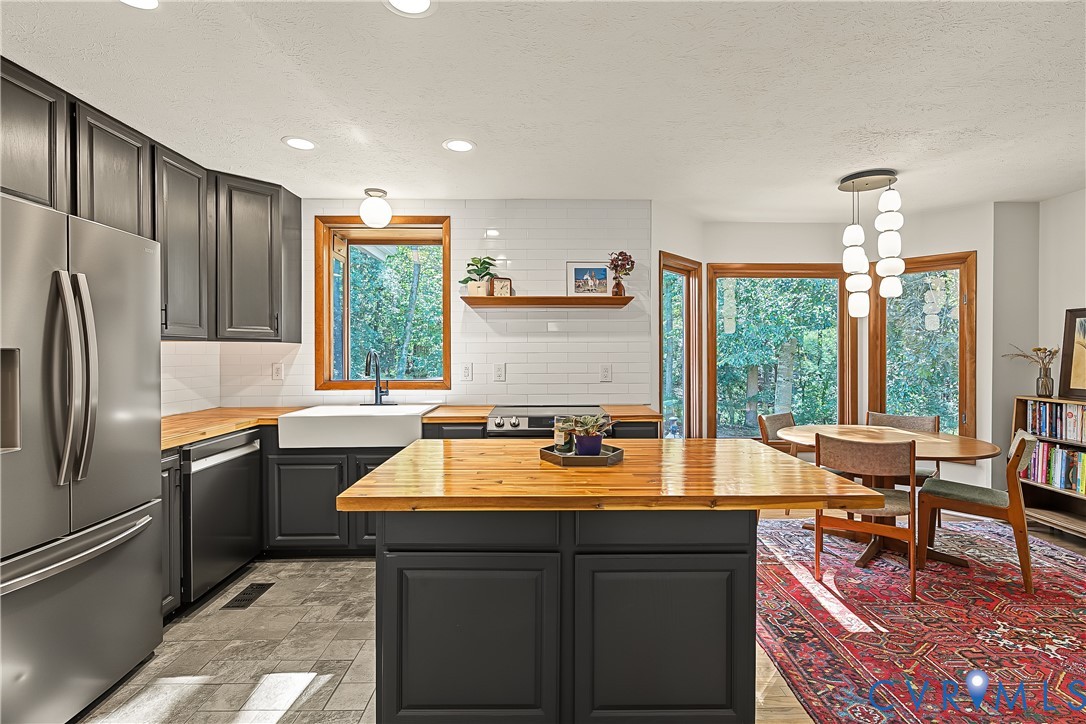 Kitchen featuring dark cabinetry, butcher block countertops, white subway tile backsplash, farmhouse-style apron sink, and a central kitchen island