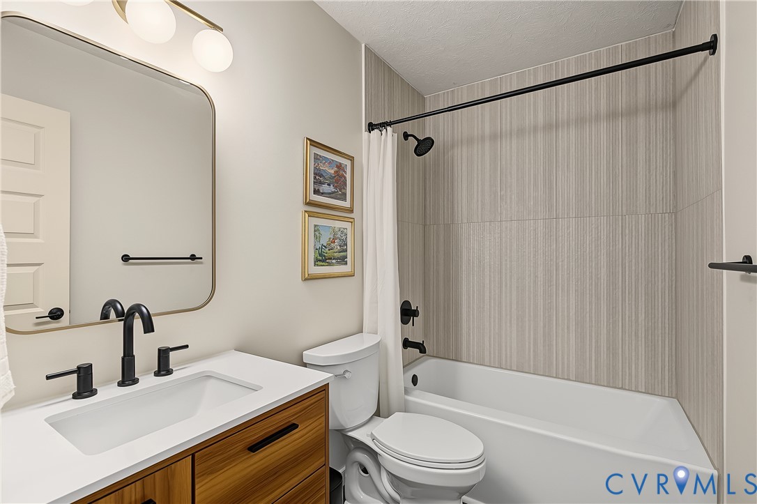 Bathroom featuring a wood-finish vanity with a rectangular sink, quartz countertop, matte black fixtures, and a shower-tub combination with vertical tile surround