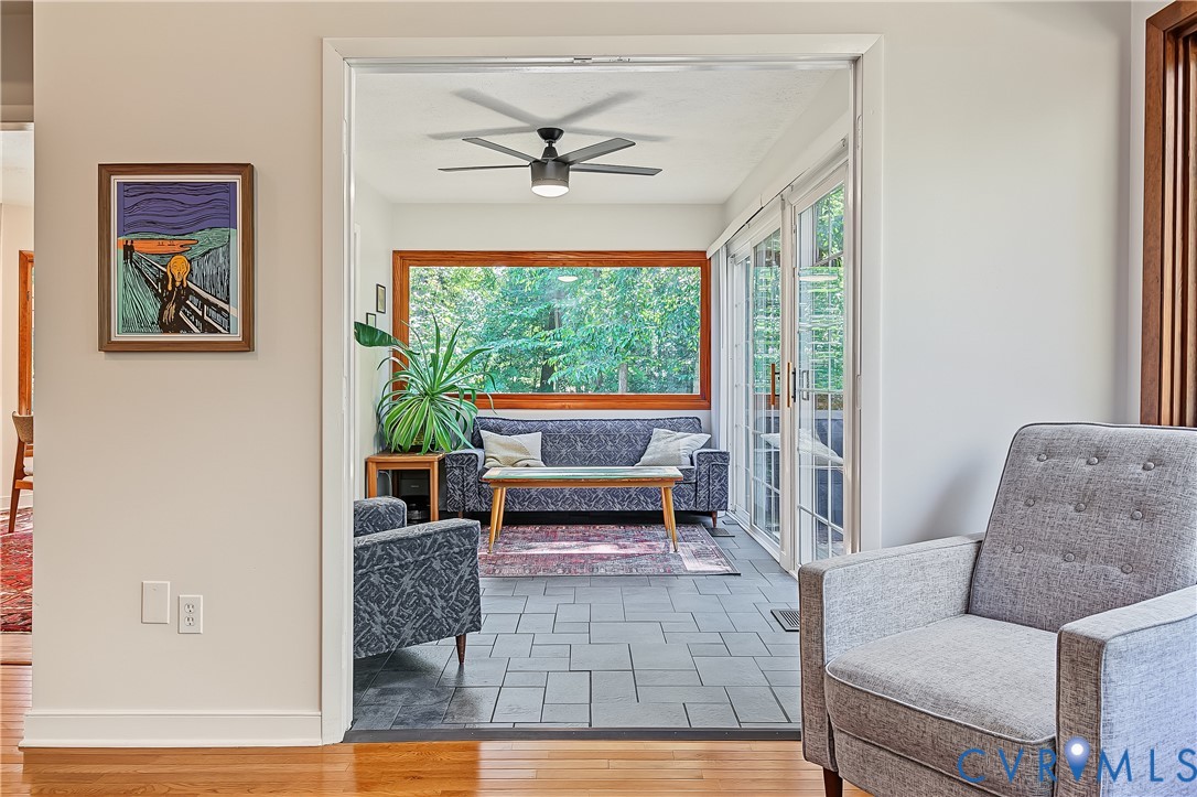 Sunroom featuring slate tile flooring, a large picture window, sliding glass doors, and a ceiling fan