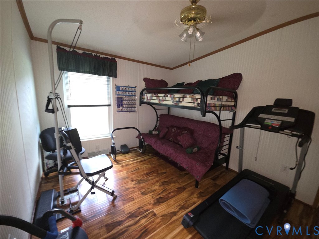 Interior room featuring wood-finish flooring, vertical panel wall detailing, and a multi-light brass ceiling fan