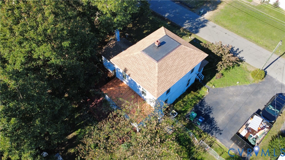 Aerial perspective of a detached residence featuring a hip roof with asphalt shingles, a flat roof section, a chimney, and a multi-level deck