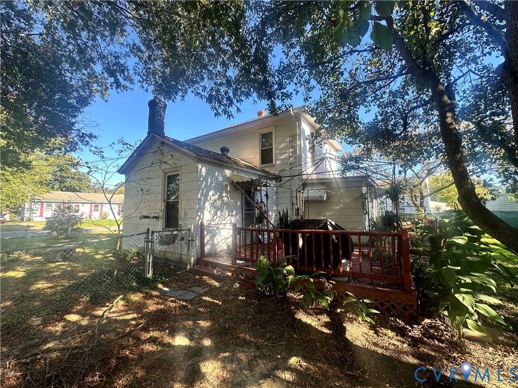 Two-story exterior featuring white horizontal siding, a brick chimney, a raised wooden deck with railings, and mature surrounding trees