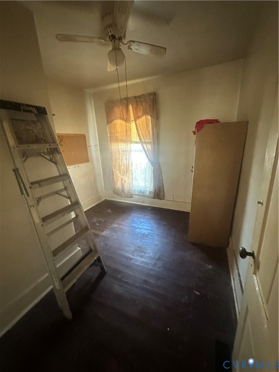 Interior room featuring dark wood-finish flooring, a ceiling-mounted fan, and a single window with an integrated blind