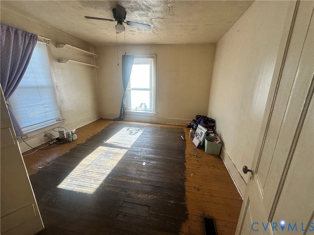 Interior room featuring exposed original hardwood flooring, two double-hung windows, and a ceiling fan with integrated lighting