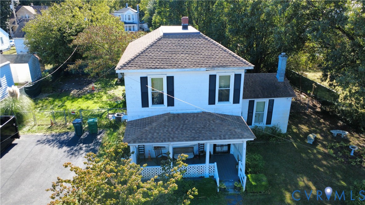 Two-story detached home featuring a hipped roof, covered front porch with lattice skirting, asphalt-paved driveway, and exterior chimney