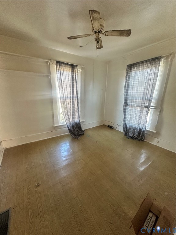 Room featuring wood-finish flooring, two windows with traditional casings, and a ceiling-mounted fan