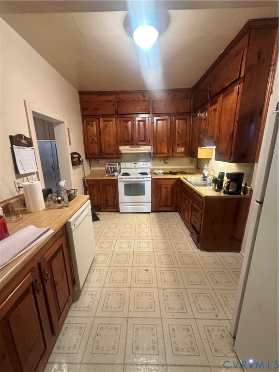 Kitchen featuring stained wood cabinetry, white electric range, integrated range hood, double-basin sink, and patterned vinyl flooring