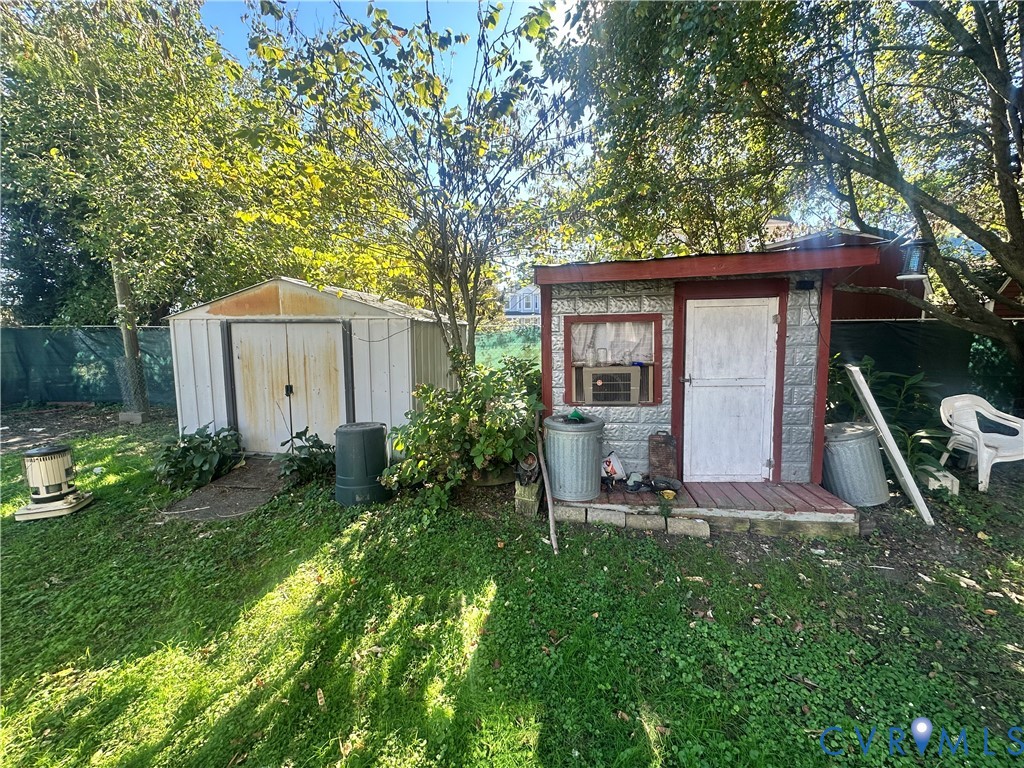 Rear yard featuring two storage structures, including a metal-sided shed and a frame outbuilding with a porch, surrounded by mature trees