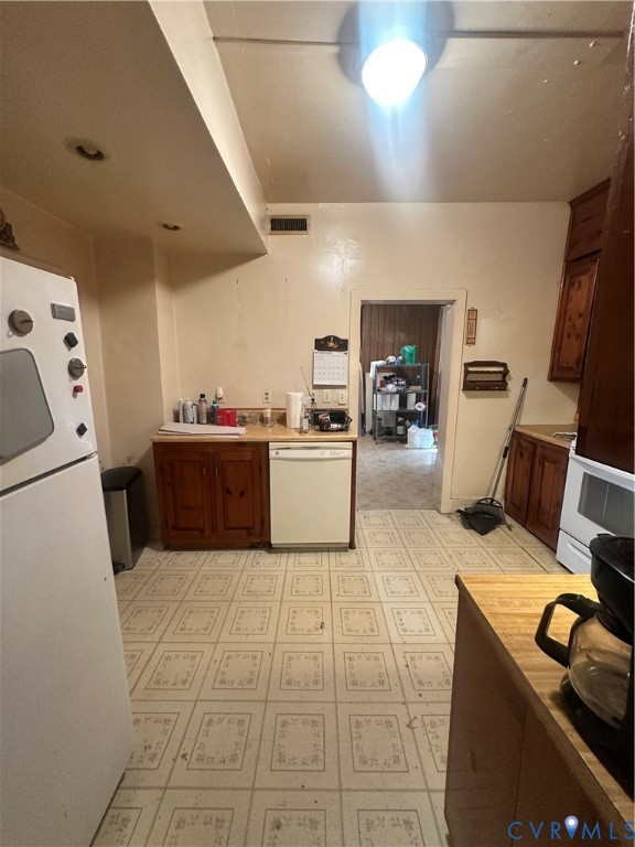 Kitchen featuring wood cabinetry, integrated dishwasher, solid surface countertops, and patterned tile flooring