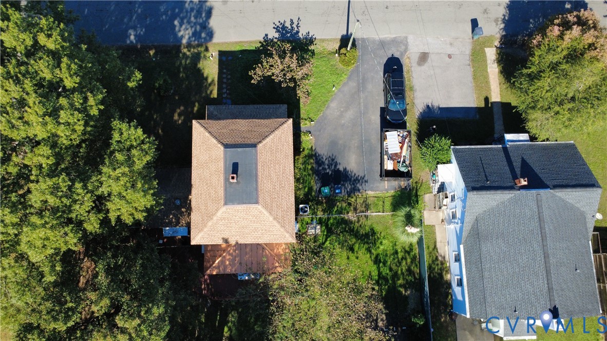 Aerial perspective featuring a multi-level asphalt shingle roof, a dedicated paved driveway, and mature trees situated on the property grounds