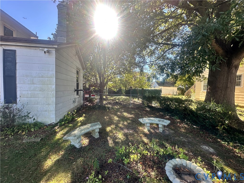 Rear yard featuring mature trees, concrete masonry benches, a circular stone fire pit, and chain-link perimeter fencing