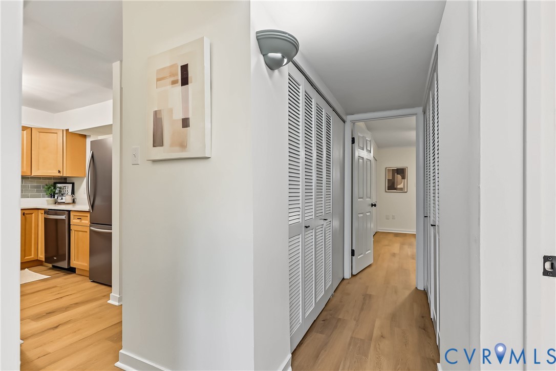 Hallway featuring wood-finish flooring, dual sets of floor-to-ceiling louvered closet doors, and wall-mounted sconce lighting