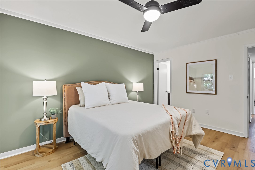 Room interior featuring a sage green accent wall, wood-finish flooring, and a modern ceiling fan with an integrated light fixture