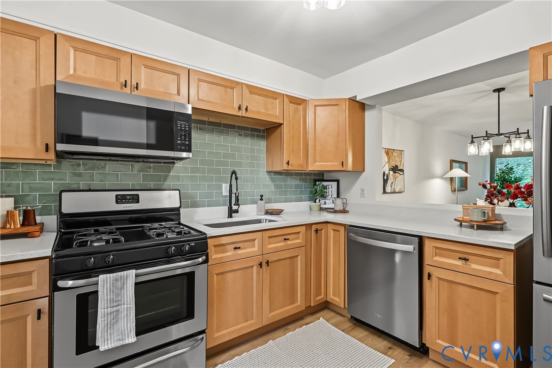 Kitchen featuring light wood cabinetry, stainless steel appliances, a green subway tile backsplash, solid-surface countertops, and a matte black gooseneck faucet