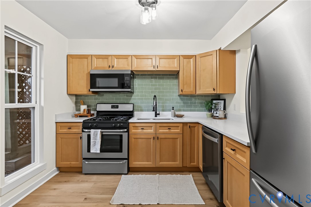 Kitchen featuring shaker-style wood cabinetry, stainless steel appliances, white solid-surface countertops, sage green subway tile backsplash, and wood-finish flooring